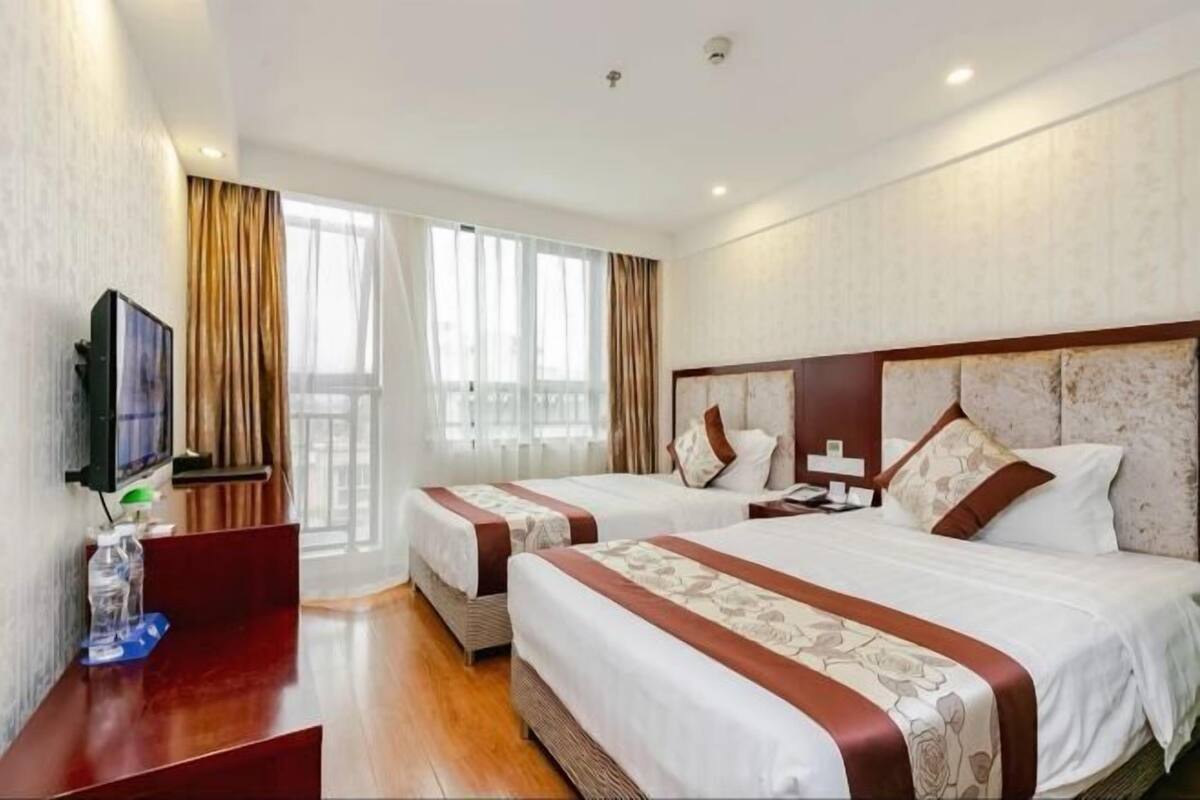 A hotel room with two beds, a TV, a desk, and a window with curtains.