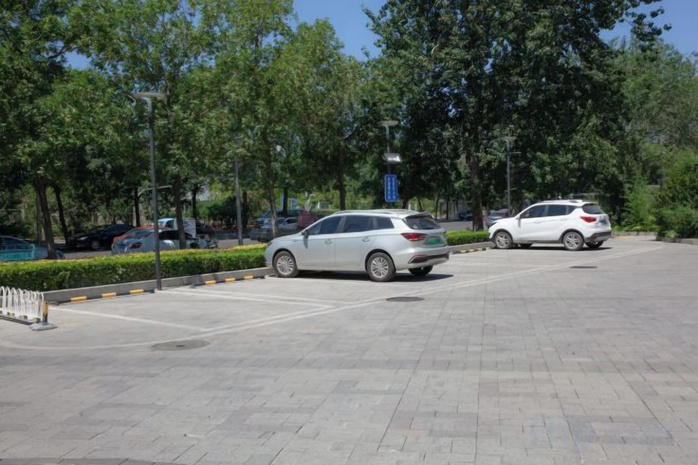 A parking lot with two cars, trees, and a clear sky.