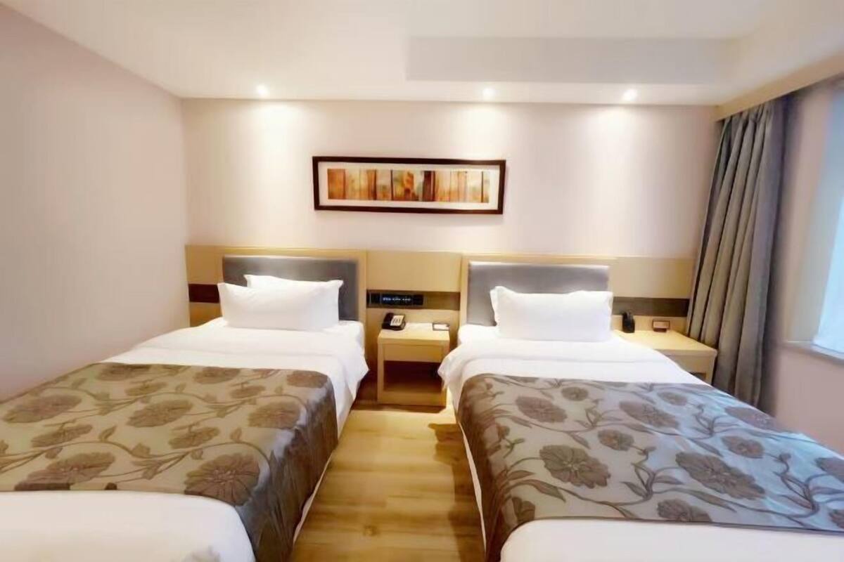 Une chambre d’hôtel avec deux lits, une table de chevet avec un téléphone et un tableau au mur.
