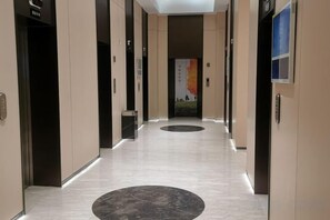 A hallway with elevators, a patterned floor, and a poster on the wall. - Jinfeng Hotel (Beijing)