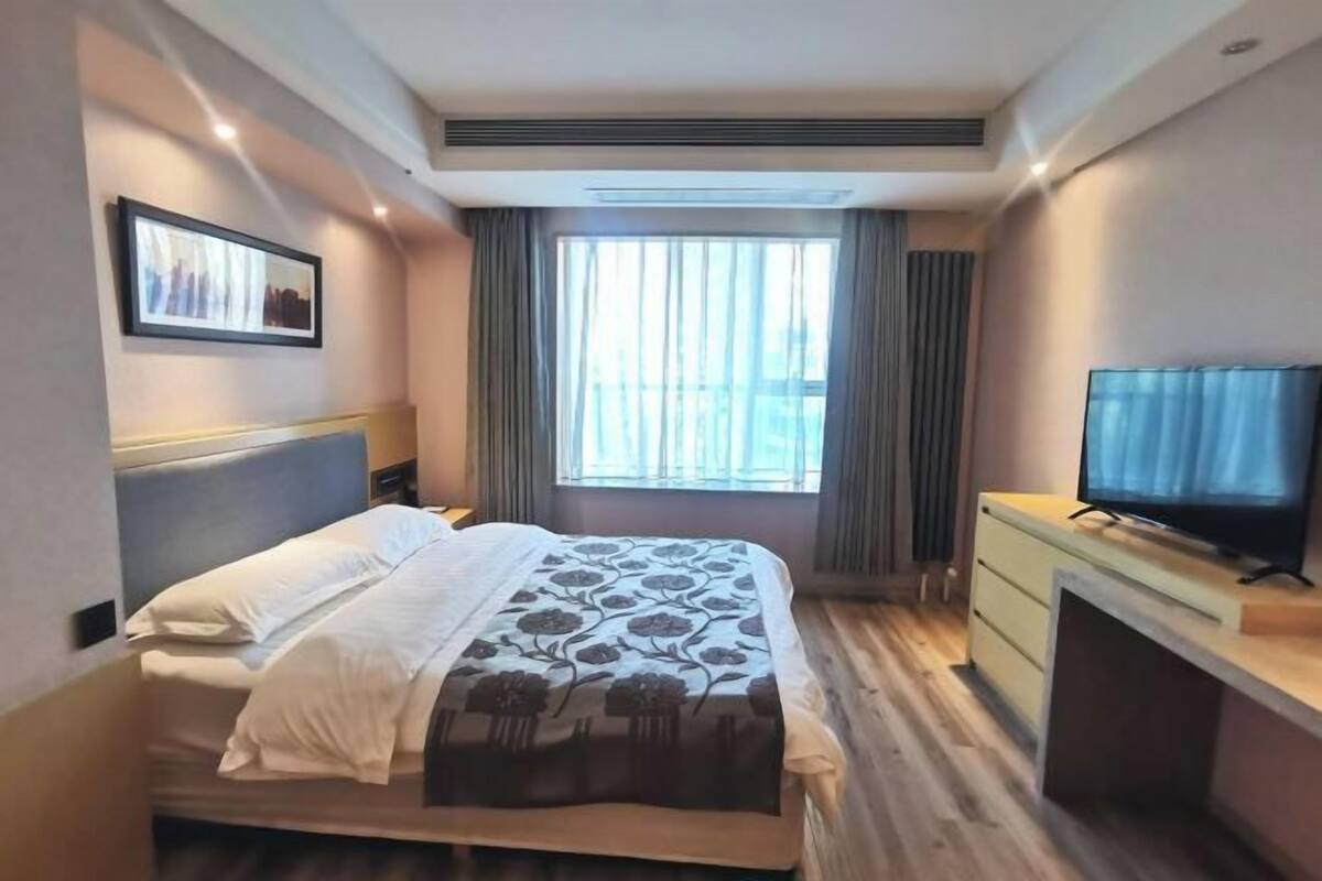 Une chambre d’hôtel avec un lit, un bureau avec une télévision, une fenêtre avec des rideaux et un tableau encadré au mur.