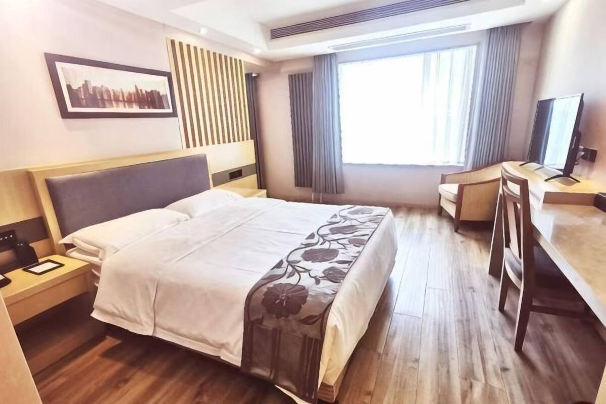 Une chambre d’hôtel avec un lit, un bureau, une chaise, une télévision et une fenêtre avec des rideaux.