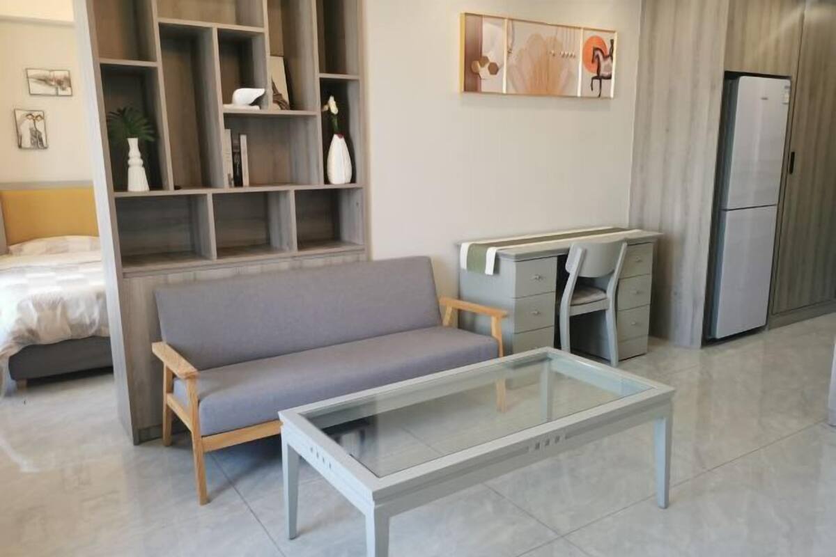 Un salon moderne comprenant un canapé, une table basse en verre, un bureau avec des tiroirs et une bibliothèque intégrée.