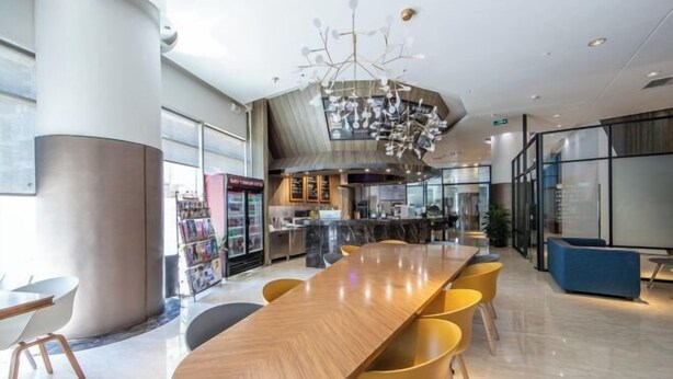 Eine moderne Hotelhalle mit einem langen Holztisch, gelben Stühlen, einem außergewöhnlichen Kronleuchter und einer Glastrennwand.