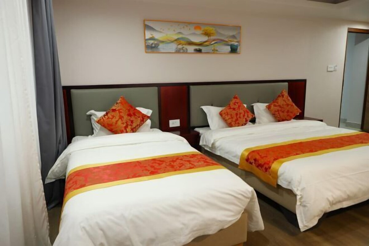 A hotel room with two beds, each with white bedding and orange accents, a painting above the beds, and a wooden headboard.