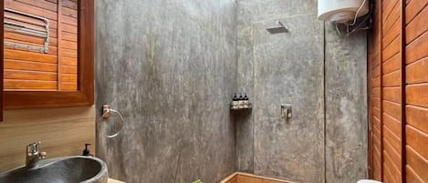 A bathroom with a stone sink, wooden cabinets, a toilet, and a shower.