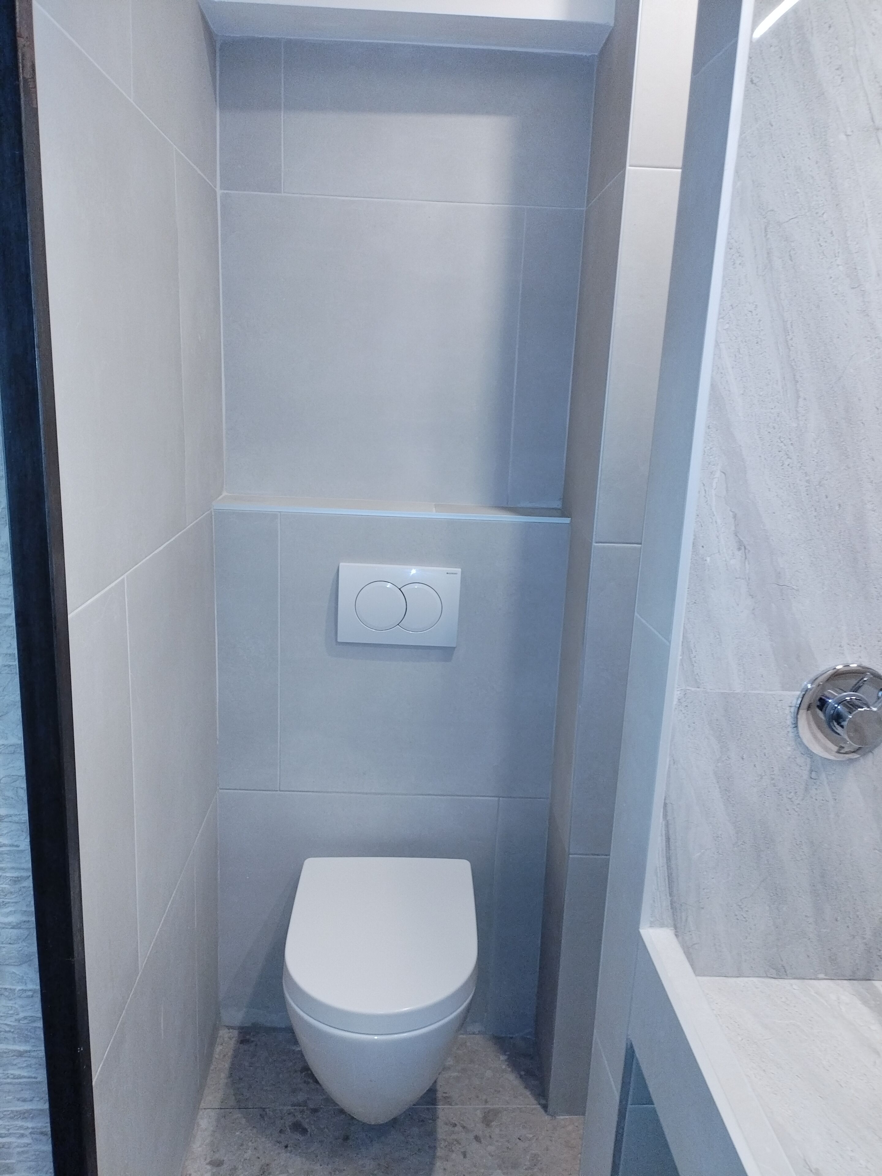 Un baño pequeño y moderno con inodoro, panel de control en la pared y zona de ducha.