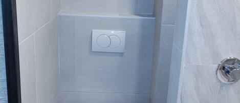 Un baño pequeño y moderno con inodoro, panel de control en la pared y zona de ducha.