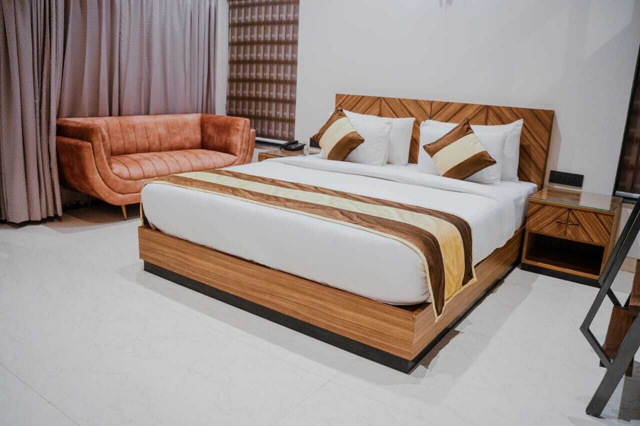 A modern hotel room with a large bed, a wooden headboard, a leather armchair, and a wooden nightstand.
