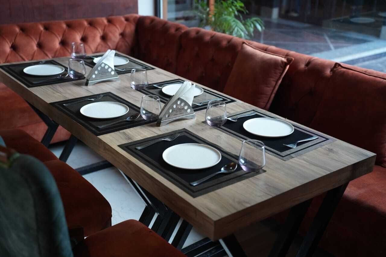 A dining table set with plates, cutlery, and glasses, surrounded by red velvet chairs.