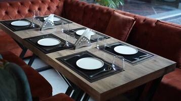 A dining table set with plates, cutlery, and glasses, surrounded by red velvet chairs.