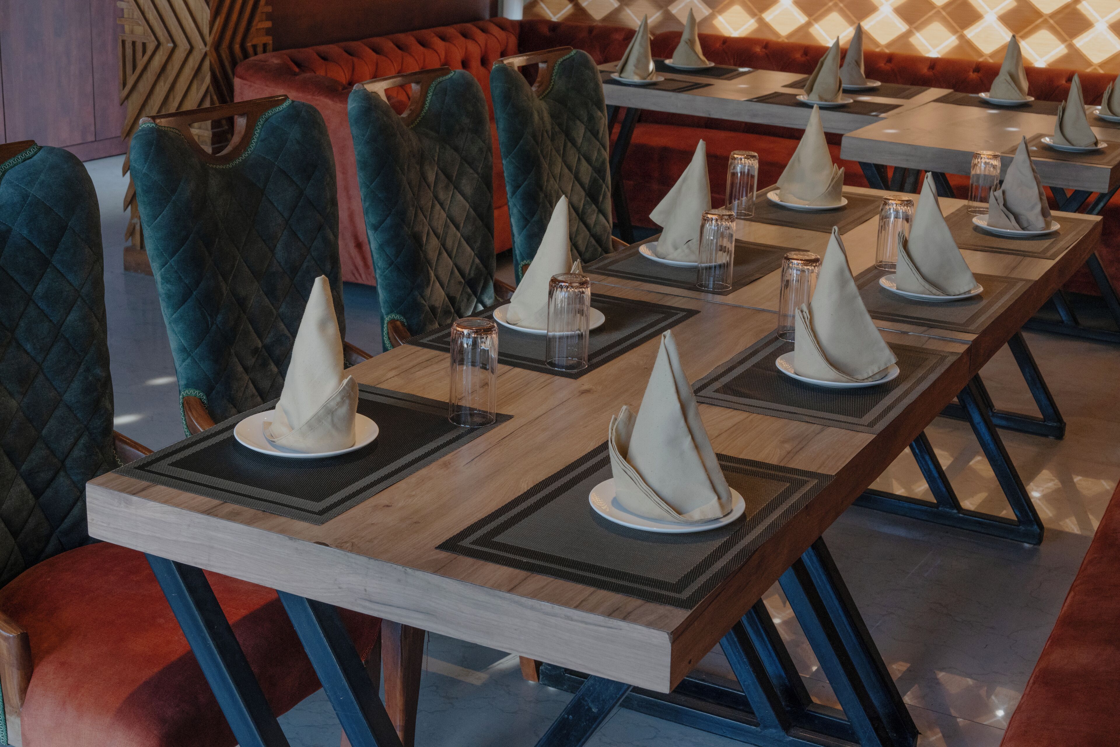 A restaurant with long wooden tables set with white napkins, clear glasses, and red upholstered chairs.