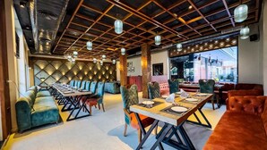 A modern dining area with a long table, cushioned seating, and a geometric ceiling design.