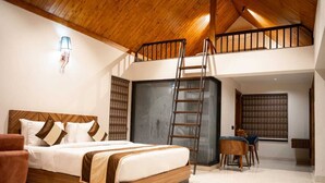A bedroom with a loft-style design, featuring a wooden ceiling, a bed with a headboard, a ladder to the upper level, and a seating area with chairs.