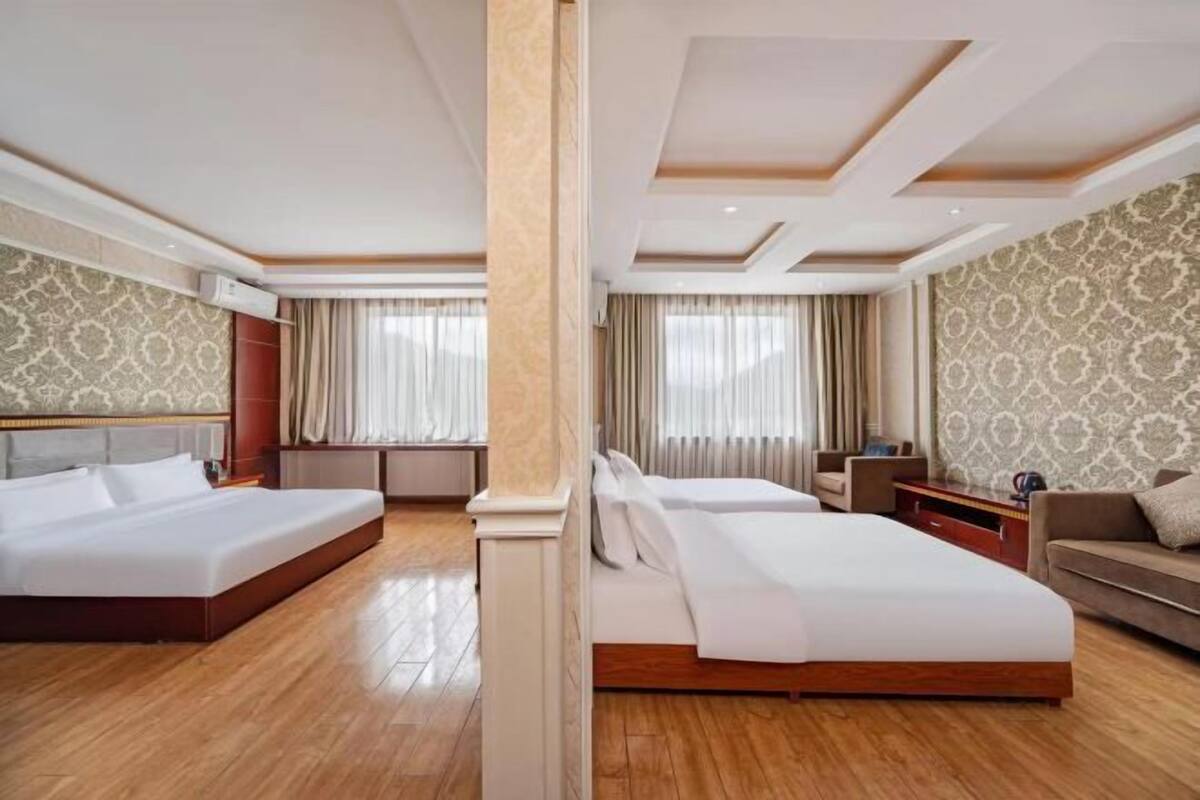 A hotel room with two beds, a sofa, a nightstand, and a patterned wallpaper.
