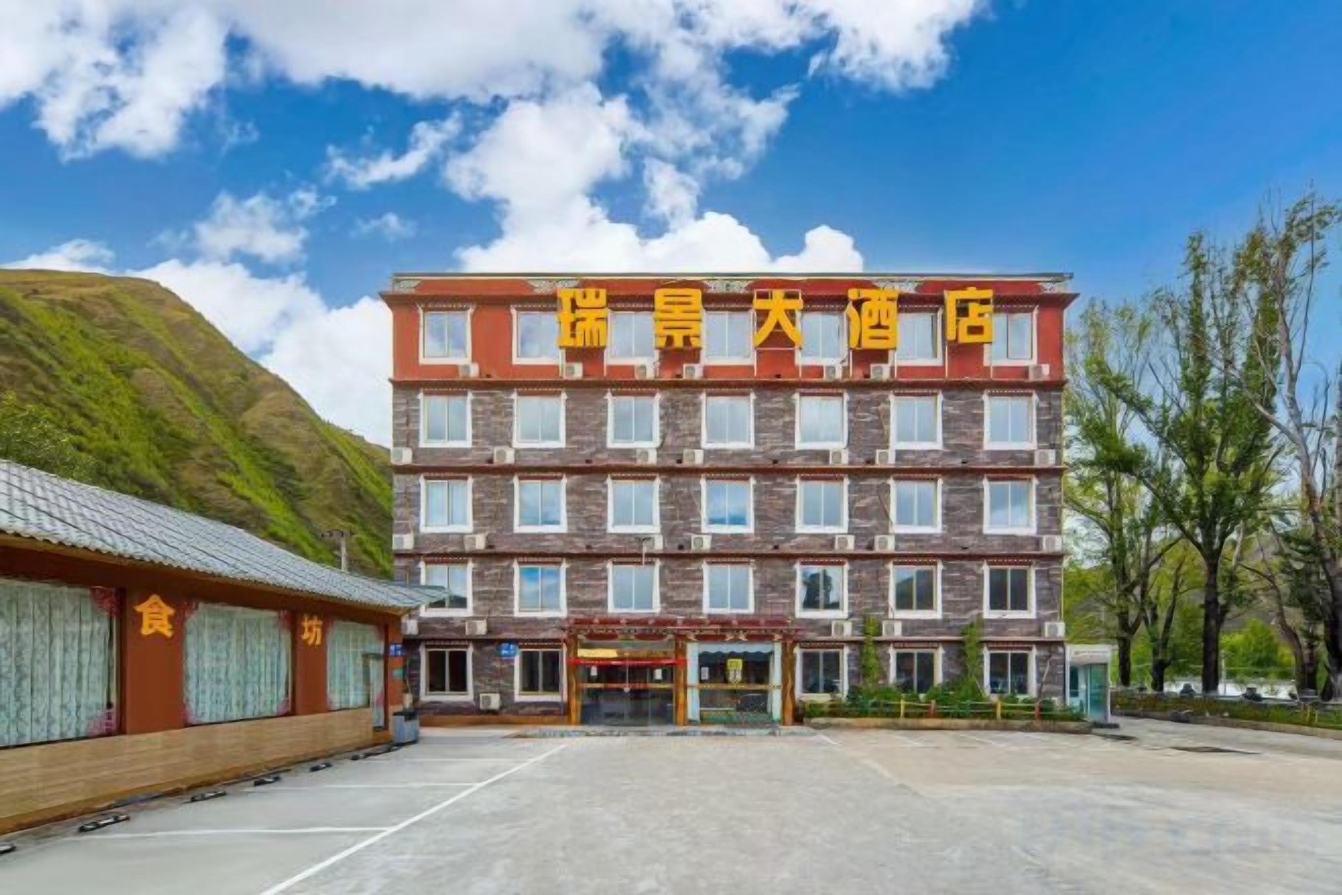 A multi-story hotel with a prominent sign, a parking lot, and a hilly landscape in the background.