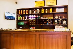 A reception area with a wooden counter, shelves with various bottles and containers, and a television mounted on the wall. - Ruijing Hotel (Kangding)