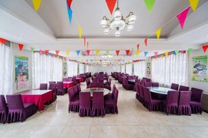Un amplio salón de banquetes con mesas redondas y sillas moradas, decorado con llamativos banderines triangulares.
