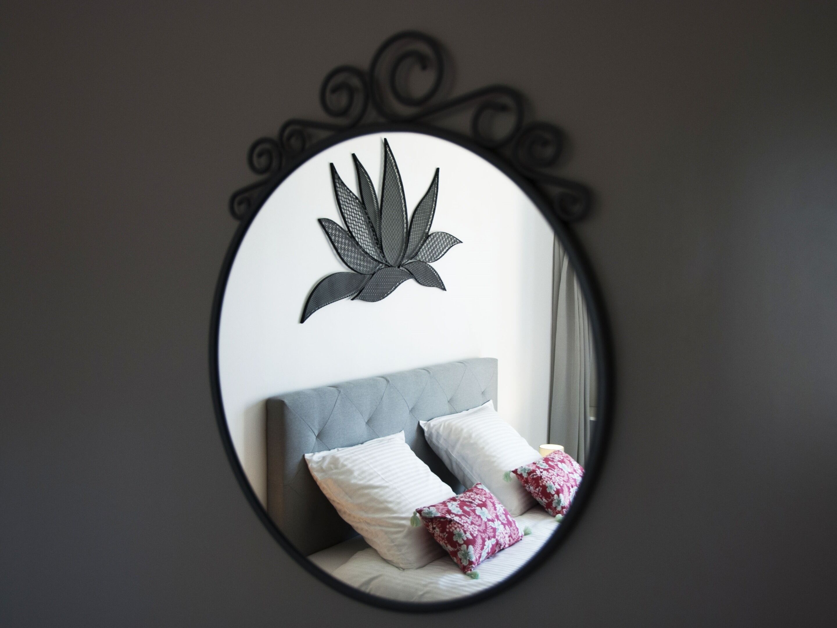 Un dormitorio con un espejo redondo, una cama con dos almohadas y un adorno en la pared.