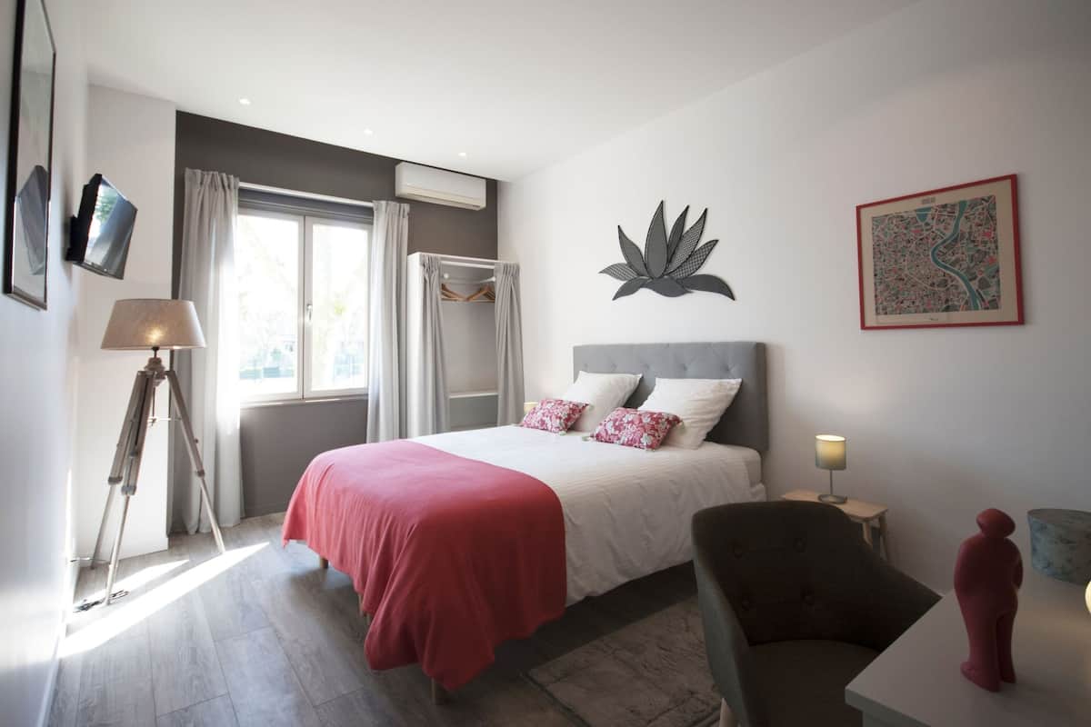 A modern bedroom with a bed, a chair, a desk, and a window with curtains.