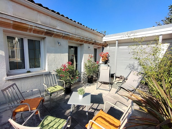 An outdoor patio area with a table and chairs, potted plants, and a view of a building with a tiled roof. - La Chartreuse-Bordeaux (Bordeaux)