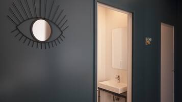 A bathroom with a modern design, featuring a wall-mounted mirror, a sink, and a shower area.