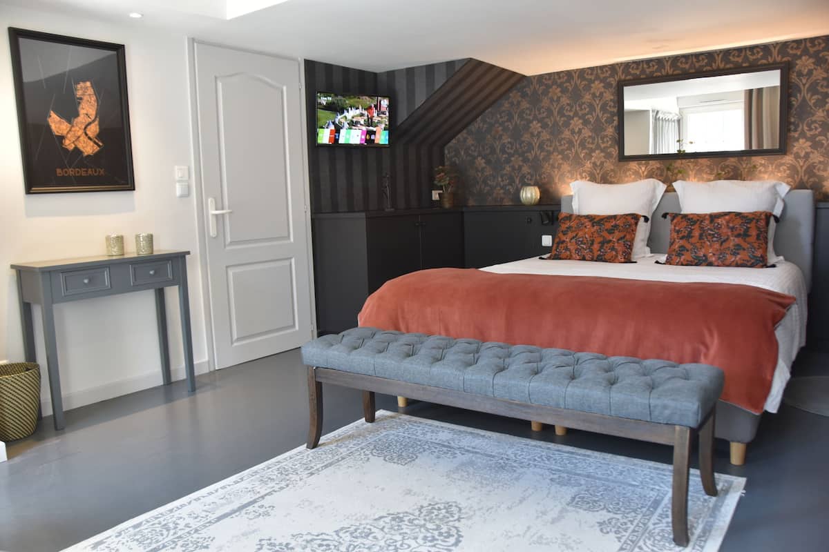 A bedroom with a bed, a bench, a TV, a dresser, and a framed picture on the wall.