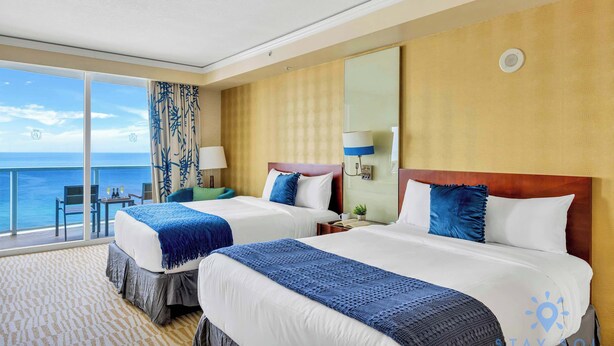 A hotel room with two beds, a balcony with a view of the sea, and a large mirror on the wall. - Deluxe Studio, Ocean View, Premium Amenities (Sunny Isles Beach)