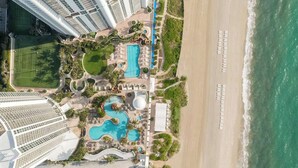 A resort with multiple swimming pools, a beach, and high-rise buildings in the background. - Deluxe Studio, Ocean View, Premium Amenities (Sunny Isles Beach)