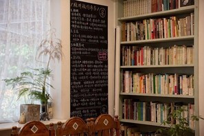 A room with a bookshelf, a window with plants, and a blackboard with text. - Jiuyueji Guesthouse (Hangzhou)