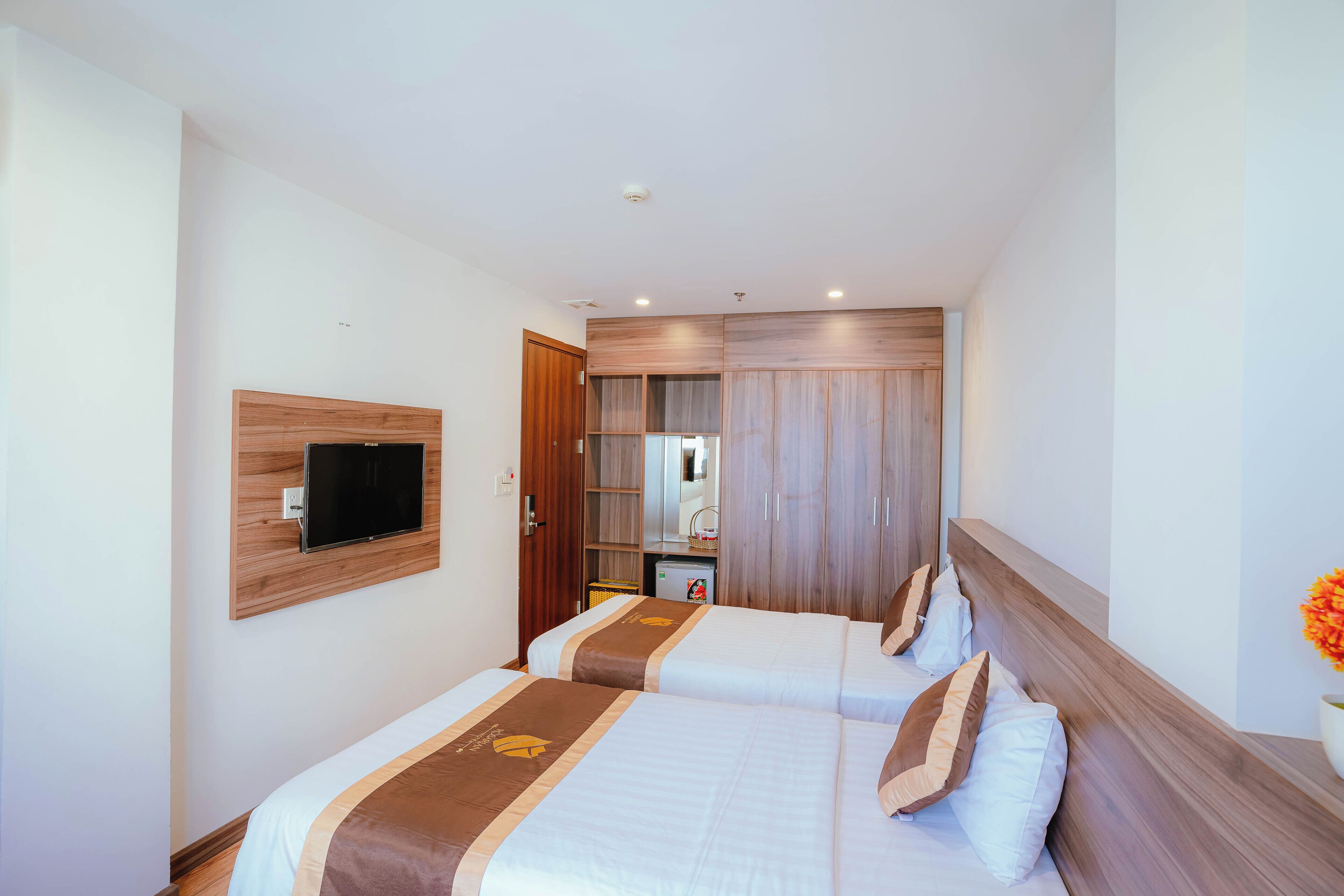 Una habitación de hotel con dos camas, un televisor montado en la pared, un armario y una pequeña cocina.