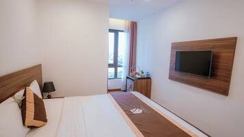 Una camera d'albergo con un letto, una televisione fissata al muro, un comodino con una lampada e una finestra con tende.