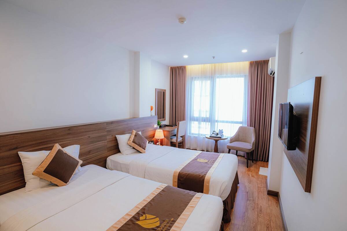 A hotel room with two beds, a TV, a desk with a chair, and a window with curtains.