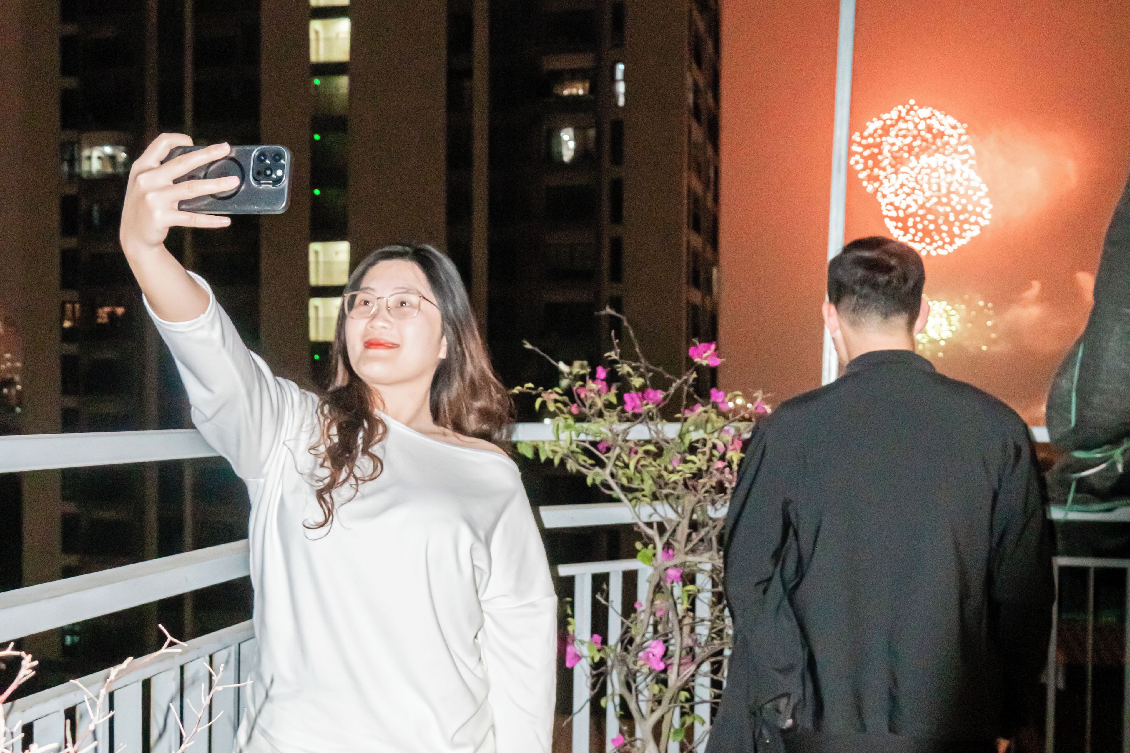 A person taking a selfie with a smartphone, a railing, and a building in the background.