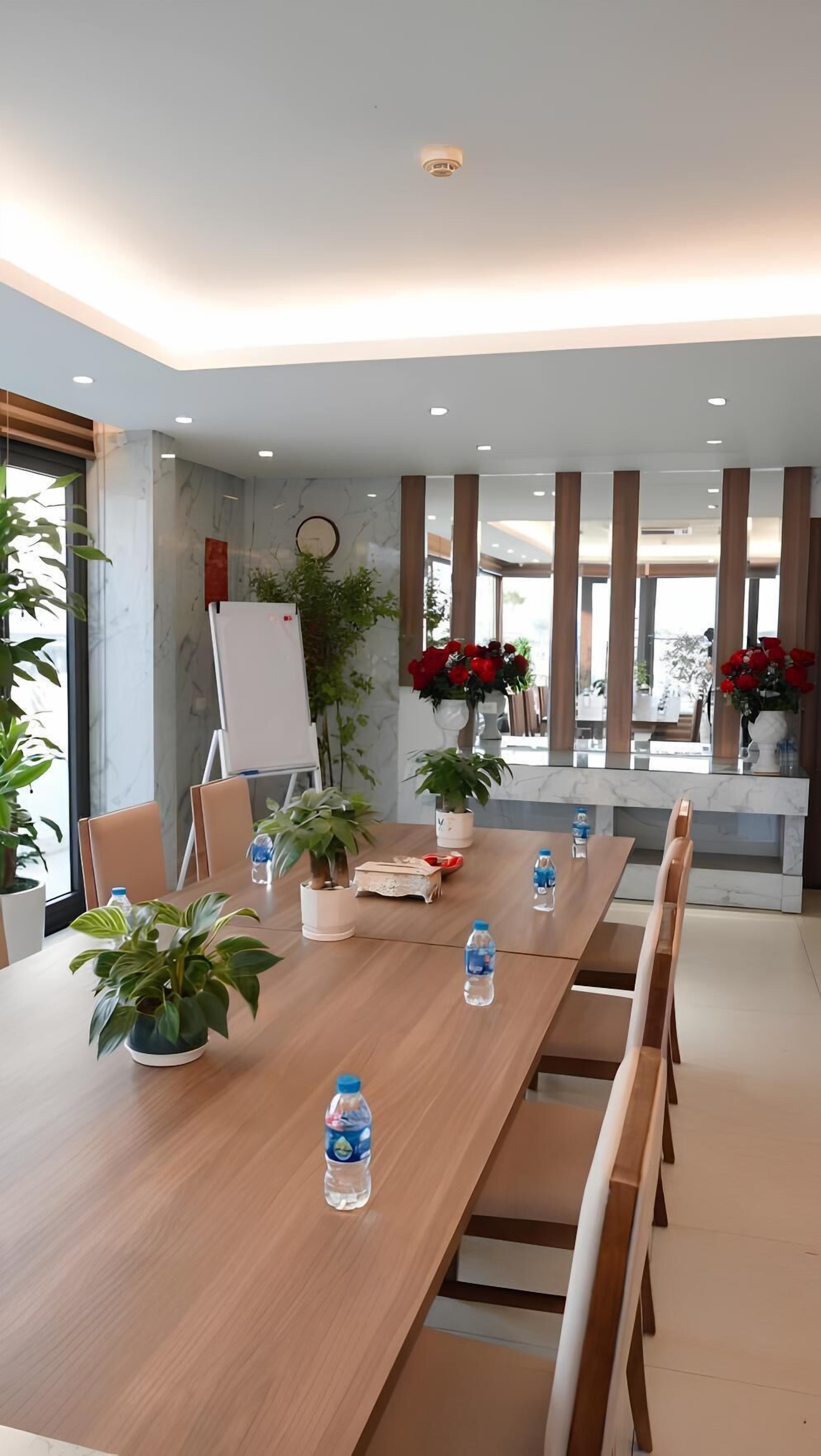 A modern meeting room with a long table, chairs, potted plants, and a whiteboard.