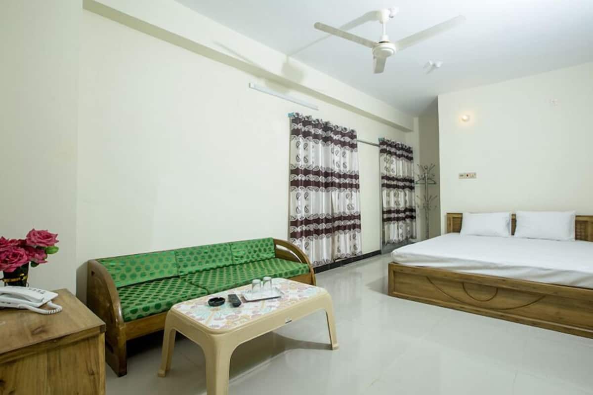 A bedroom with a bed, a sofa, a small table, a ceiling fan, and a window with curtains.