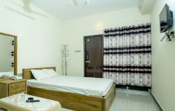 A bedroom with a bed, a bedside table with a phone and a remote, a mirror, a wardrobe, and a curtain. - Resort Rain View Hotel Cox's Bazar (Cox's Bazar)