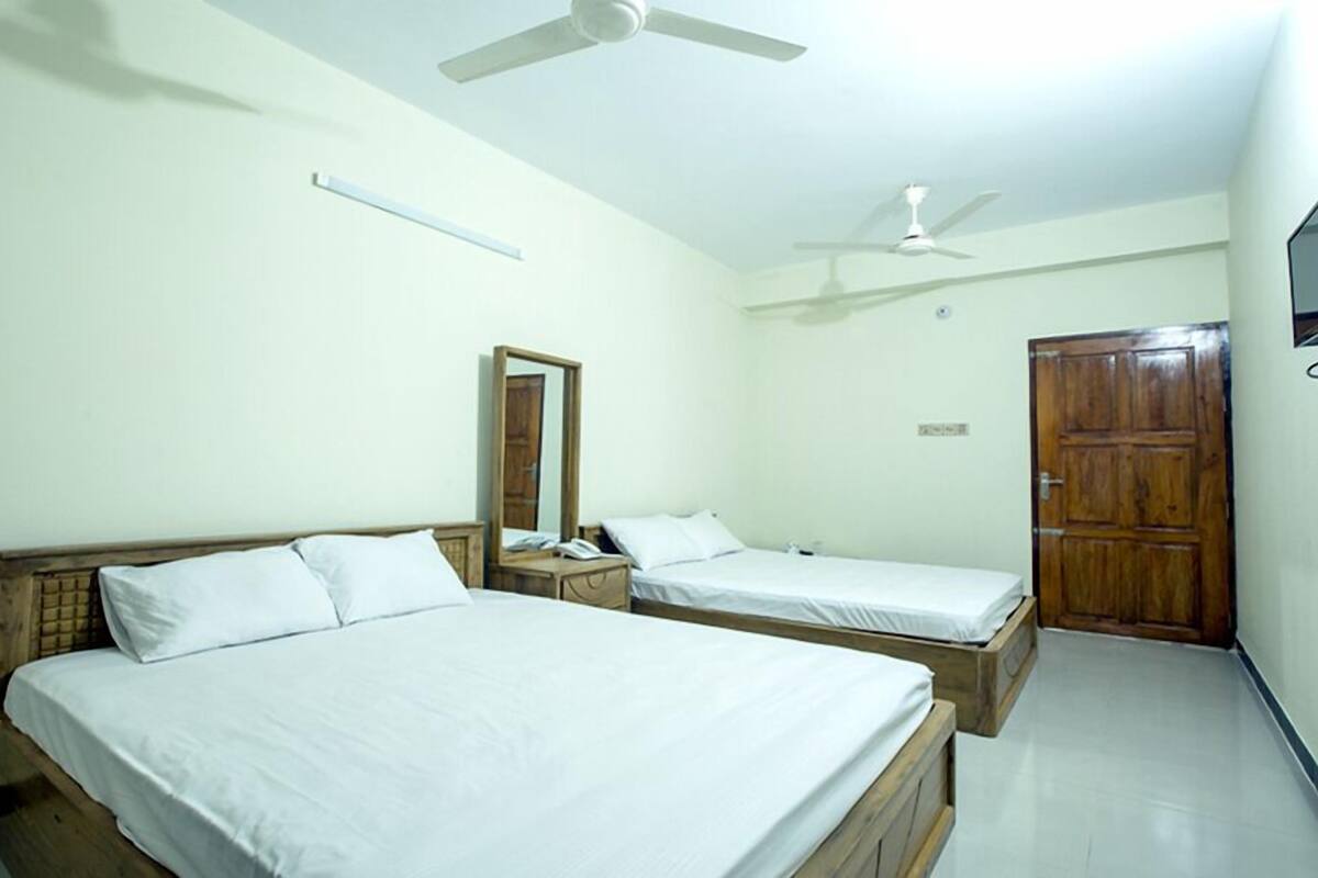 A room with two beds, a ceiling fan, a wooden door, and a mirror on the wall.
