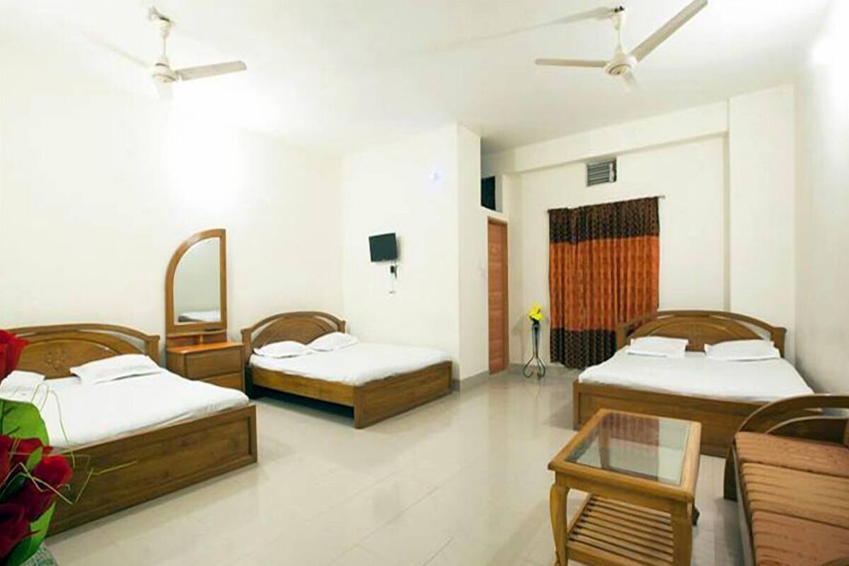 A hotel room with two single beds, a small table, and ceiling fans.