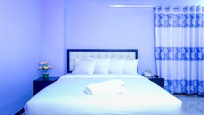 A hotel room with a neatly made bed, a bedside table with a phone, and a nightstand with a vase of flowers. - Resort Rain View Hotel Cox's Bazar (Cox's Bazar)