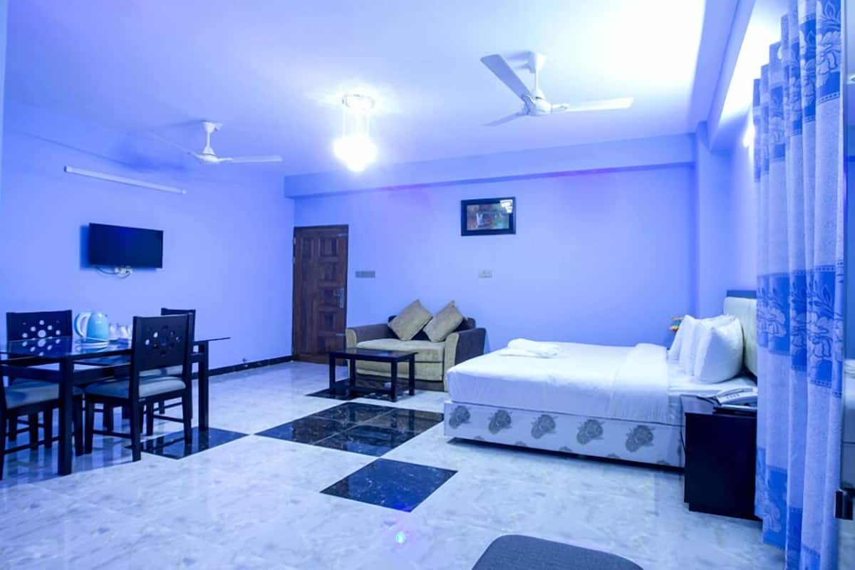 A room with a bed, a sofa, a dining table with chairs, a television, and ceiling fans.