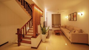 A modern living room with a wooden staircase, a sofa, a coffee table, and a potted plant. - The Grand Bliss, Kottawa, 3-bedroom villa with AC, WiFi, Private Pool, and Gym (Pannipitiya, Kottawa)