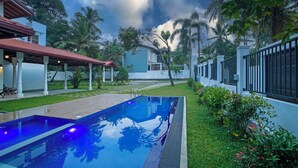 A swimming pool with a clear view of the surrounding area, including a covered seating area and a modern building with a red roof. - The Grand Bliss, Kottawa, 3-bedroom villa with AC, WiFi, Private Pool, and Gym (Pannipitiya, Kottawa)