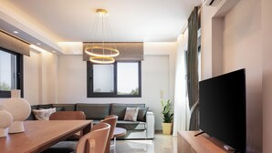Una sala de estar moderna con una mesa de comedor de madera, sillas, un sofá, un televisor de pantalla plana y un gran ventanal.
