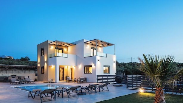 Una casa moderna de dos pisos con piscina, mobiliario exterior y un patio bien iluminado.