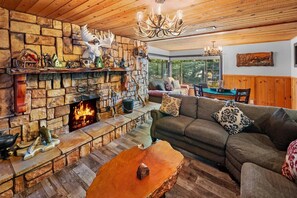 A cozy living room with a stone fireplace, a wooden ceiling, and a comfortable sofa.