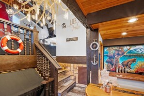 A wooden staircase with a life preserver, a wall with a 'Life is better at Lake' sign, and a painting of a bear and a dog by a lake. - Lake Pointe Retreat By Destination Big Bear:Close to Village and Marina! Hot Tub! Pool Table! Shuffleboard! Air Hockey! Fully Fenced Yard! Pet Friendly! (Big Bear Lake)