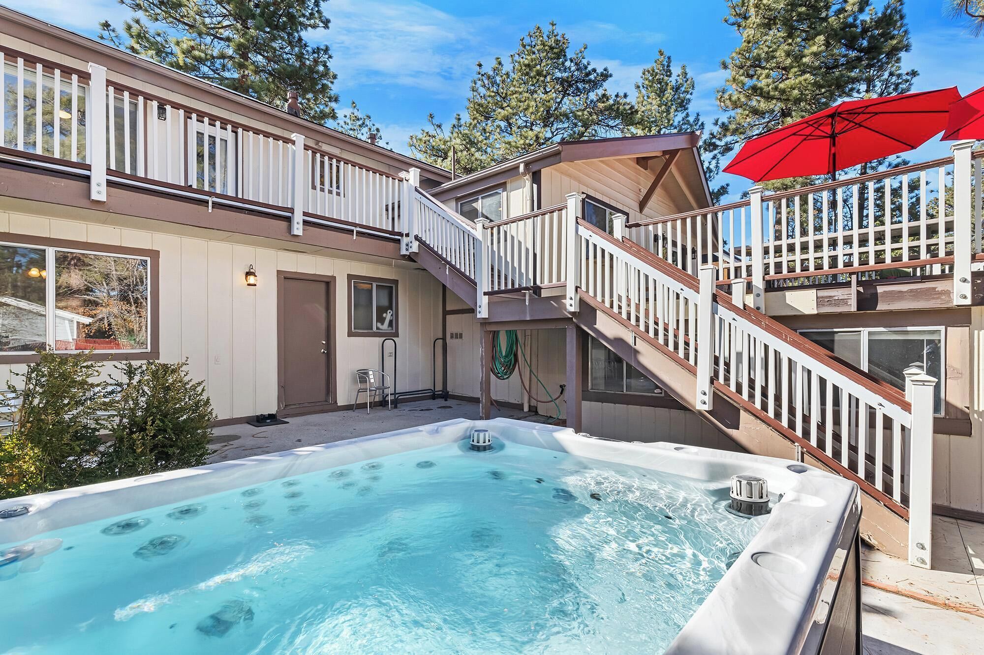 A two-story house with a hot tub in the backyard, a staircase, and a red umbrella.