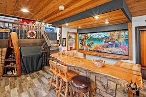 A bar area with wooden furniture, a large painting of bears, and a lifebuoy on the wall. - Lake Pointe Retreat By Destination Big Bear:Close to Village and Marina! Hot Tub! Pool Table! Shuffleboard! Air Hockey! Fully Fenced Yard! Pet Friendly! (Big Bear Lake)