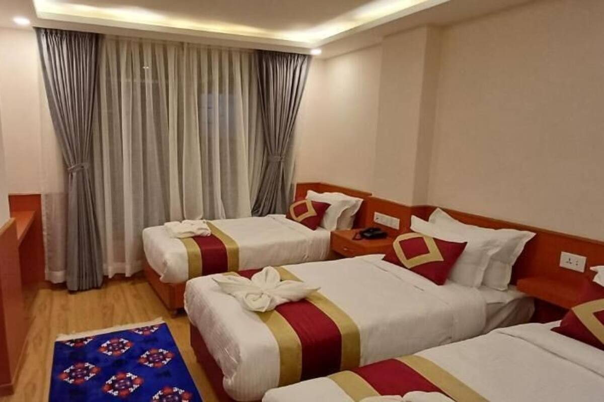 A hotel room with two beds, a TV, a desk, and a window with curtains.